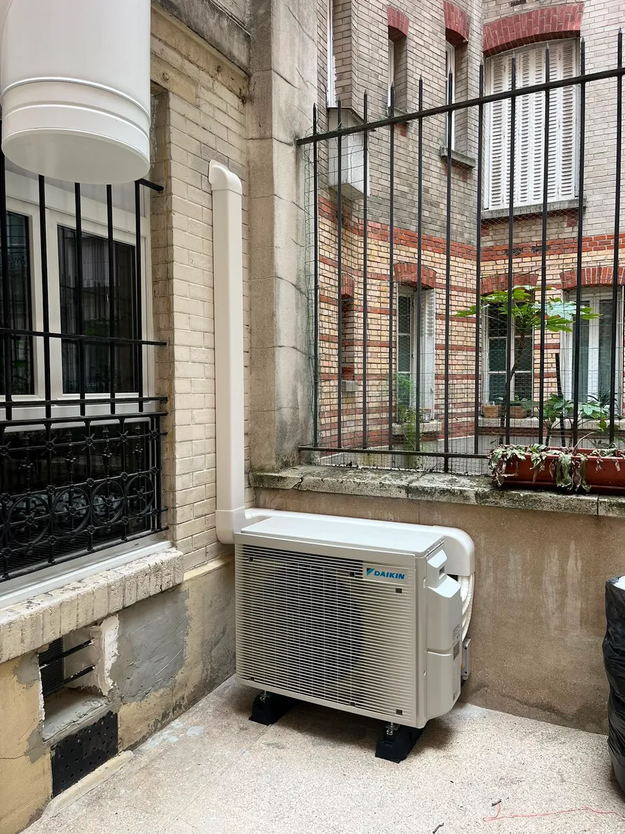 Unité extérieure de climatisation posée dans une cour pavée